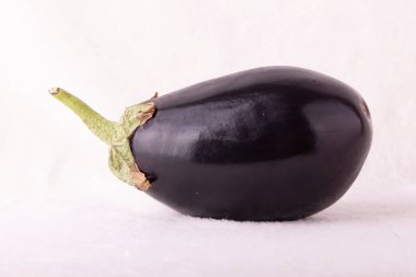 Yeşil saplı siyah bir patlıcan. Sapı yukarıya bakıyor. Patlıcan beyaz arka planda duruyor.