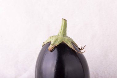Üstünde yeşil saplı siyah bir patlıcan. Sapı yukarıya bakıyor. Patlıcan beyaz arka planda duruyor.