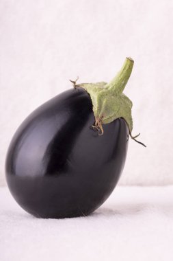 Üstünde yeşil saplı siyah bir patlıcan. Patlıcan beyaz bir yüzeyde duruyor.