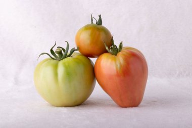 Üç domates üst üste istiflenmiş. Üstteki domates yeşil, ortası kırmızı ve alttaki de kırmızı.