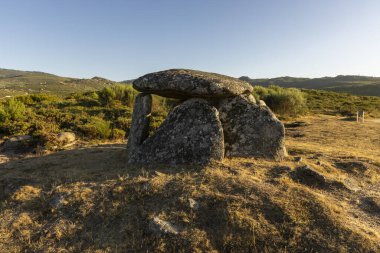 Bir tarlada yamaçta büyük bir kaya bulunur. Kaya çimenler ve ağaçlarla çevrili. Sahneye huzurlu ve huzurlu bir atmosfer veriyor.