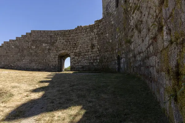 Ortasında küçük bir kemer olan taş bir duvar. Kemer yolu çimenler ve yosunlarla çevrili.