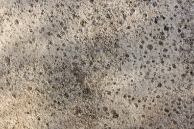 Bir sürü küçük deliği ve lekesi olan gri ve beyaz bir yüzey. Yüzey pürüzlü ve düzensiz. Görüntüde ıssız ve terk edilmiş bir his var.