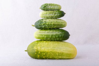 Beyaz arka planda bir yığın salatalık. Salatalıklar yeşil ve sarıdır. Tazelik ve sağIık kavramı