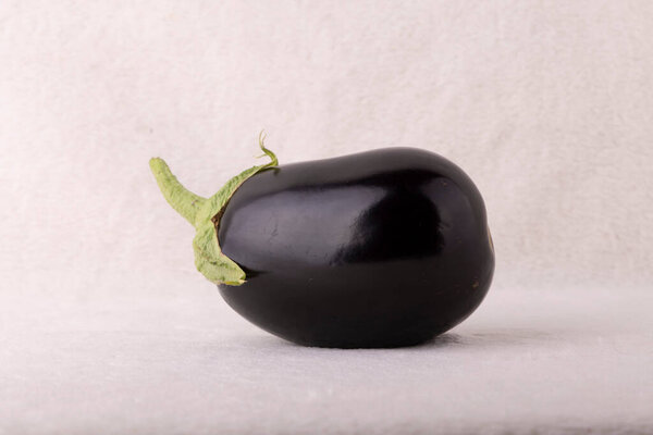 A black eggplant with a green stem is sitting on a white background. The eggplant is the main focus of the image, and it is the only object in the scene