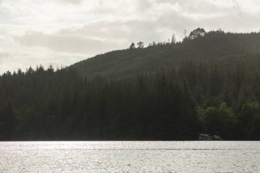 Üzerinde tekne olan bir göl ve arka planda bir dağ. Gökyüzü bulutlu ve su sakin.