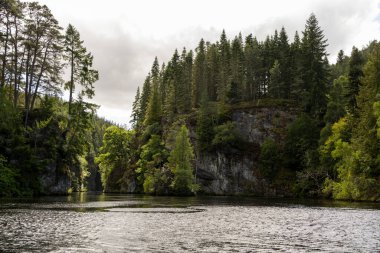 Ağaçlar ve dağlarla çevrili güzel bir göl. Su sakin ve gökyüzü bulutlu. Huzurlu ve huzurlu bir sahne.