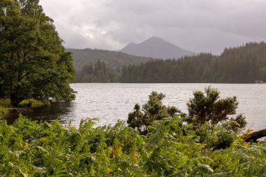 Arka planda dağ olan bir göl. Su sakin ve gökyüzü bulutlu.