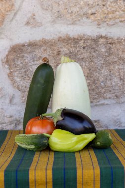 Bir masada salatalık, domates, biber ve kabak gibi çeşitli sebzeler sergilenmektedir.