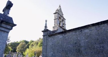 A gate with a stone wall behind a Romanesque church with a bell tower. The gate is made of metal and is open. The stone wall is grey.