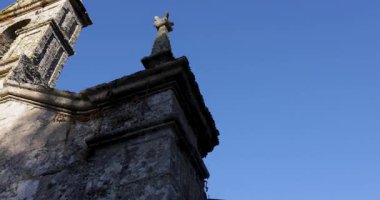 A Romanesque church steeple with a cross on top. The sky is blue and clear