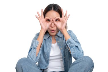 Genç Asyalı bir kadının portresi mavi kot pantolon giyer ve ellerini gözlük şeklinde yapar..