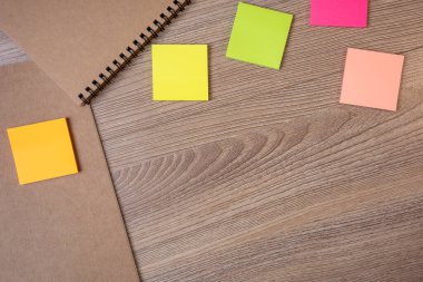 Kahverengi kapaklı ve kenarında yüzük olan defter. Üzerinde post-it olan kahverengi ahşap masaya koy.