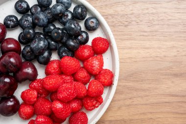 Vişne, ahududu ve böğürtlen de dahil olmak üzere karışık meyvelerin yüksek çözünürlüklü fotoğrafı bir tabakta bölünmüş odak tekniğiyle çekildi..