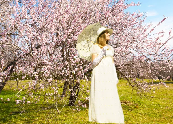 stock image Woman in white historical dress with white umbrella with pink spring trees in blossom.