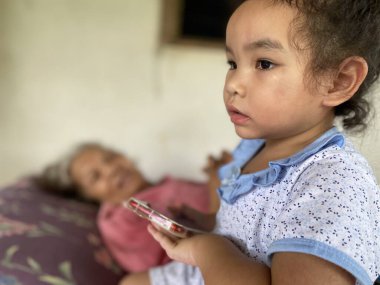 Cep telefonu olan Asyalı kız büyük büyükbabanın yanında oturuyor.