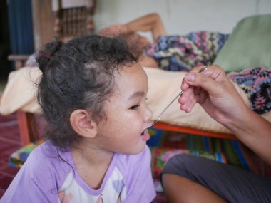 Anne evdeki oturma odasında kızını kaşıkla besliyor.