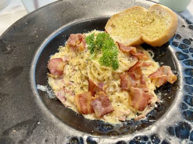 Lezzetli Carbonara soslu spagetti ve siyah tabakta parmesan peyniri.
