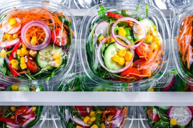Önceden paketlenmiş sebze salatalarıyla dolu plastik kutular. Ticari bir buzdolabında satılıyor.