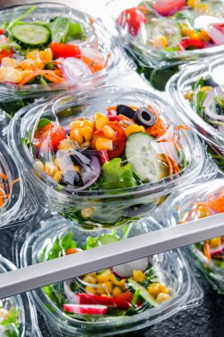Önceden paketlenmiş sebze salatalarıyla dolu plastik kutular. Ticari bir buzdolabında satılıyor.