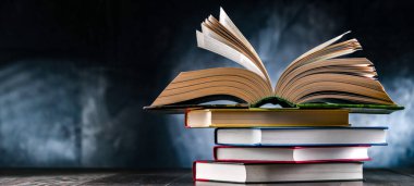 Bir yığın kitabın üzerinde açık bir kitap bulunan kompozisyon. 