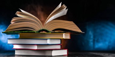 Bir yığın kitabın üzerinde açık bir kitap bulunan kompozisyon. 