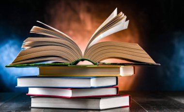 Bir yığın kitabın üzerinde açık bir kitap bulunan kompozisyon. 