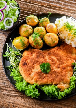 Patates ve lahana ile servis edilen ekmek kırıntılarıyla kaplı domuz pirzolası.