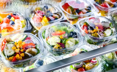 Önceden paketlenmiş meyve ve sebze salatalarıyla dolu plastik kutular ticari bir buzdolabında satılıyor.