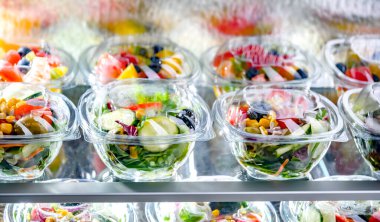 Önceden paketlenmiş meyve ve sebze salatalarıyla dolu plastik kutular ticari bir buzdolabında satılıyor.