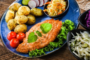 Patates ve sebze salatalı ekmek kırıntılarıyla kaplı domuz pirzolası.