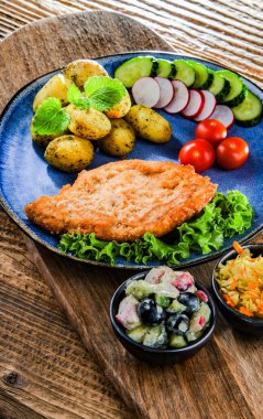 Patates ve sebze salatalı ekmek kırıntılarıyla kaplı domuz pirzolası.