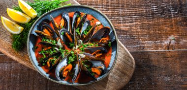 Maydanoz ve limonla servis edilen domates soslu bir tabak midye.