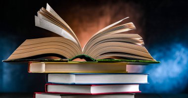 Bir yığın kitabın üzerinde açık bir kitap bulunan kompozisyon. 