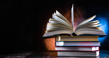 Bir yığın kitabın üzerinde açık bir kitap bulunan kompozisyon. 