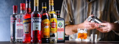 POZNAN, POL - 28 DEC 2021: Çeşitli küresel likör markaları ve kokteyl karıştırıcıyla içki hazırlayan bir barmen