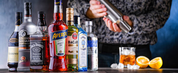 POZNAN, POL - DEC 28, 2021: Bottles of assorted global hard  liquor brands and a bartender preparing a drink with a cocktail shaker