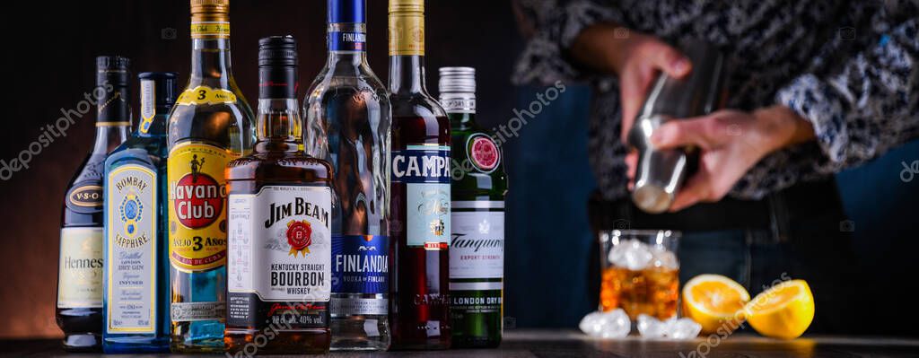 POZNAN, POL - DEC 28, 2021: Bottles of assorted global hard  liquor brands and a bartender preparing a drink with a cocktail shaker