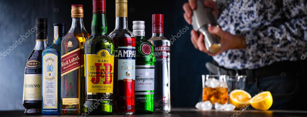 POZNAN, POL - DEC 28, 2021: Bottles of assorted global hard  liquor brands and a bartender preparing a drink with a cocktail shaker
