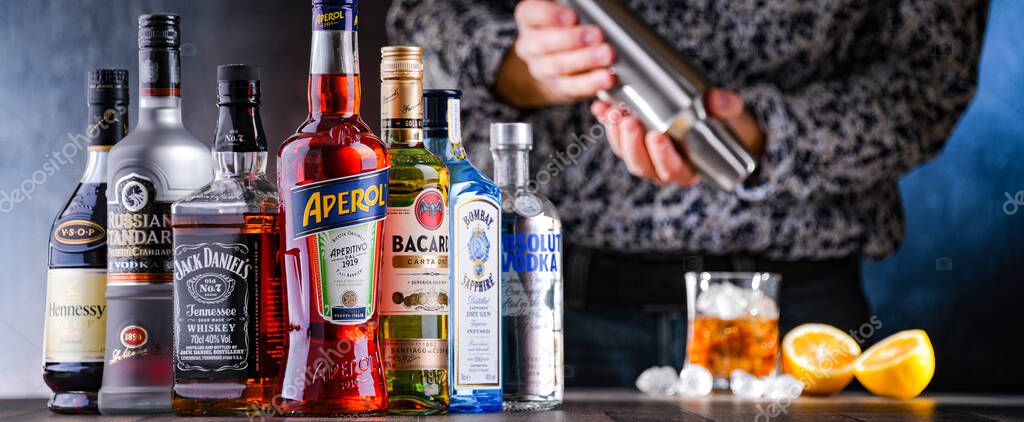 POZNAN, POL - DEC 28, 2021: Bottles of assorted global hard  liquor brands and a bartender preparing a drink with a cocktail shaker