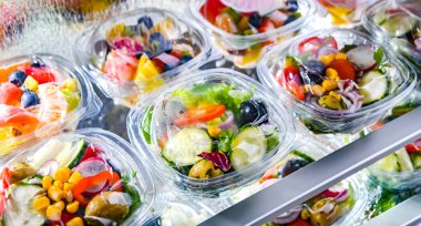 Önceden paketlenmiş meyve ve sebze salatalarıyla dolu plastik kutular ticari bir buzdolabında satılıyor.