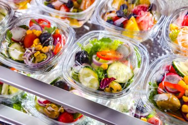 Önceden paketlenmiş meyve ve sebze salatalarıyla dolu plastik kutular ticari bir buzdolabında satılıyor.