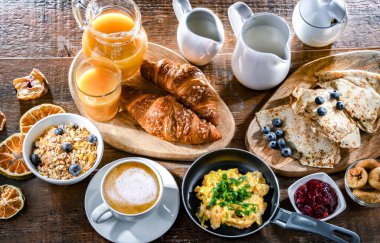 Breakfast served with coffee, orange juice, scrambled eggs, cereals, pancakes and croissants.