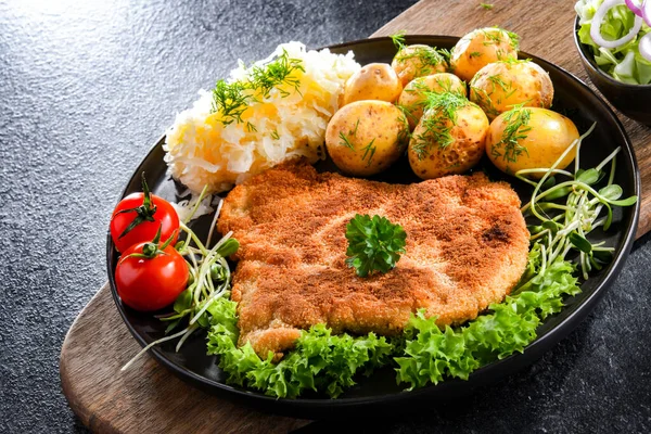 Patates ve lahana ile servis edilen ekmek kırıntılarıyla kaplı domuz pirzolası.