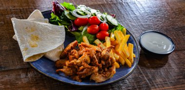 Patates kızartması, pitta ekmeği, sebze ve tzatziki ile servis edilir.