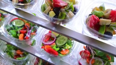 Önceden paketlenmiş meyve ve sebze salatalarıyla dolu plastik kutular ticari bir buzdolabında satılıyor.