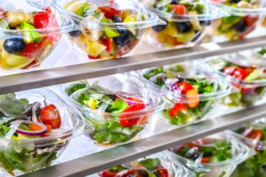Önceden paketlenmiş meyve ve sebze salatalarıyla dolu plastik kutular ticari bir buzdolabında satılıyor.