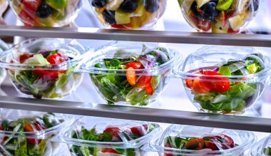 Önceden paketlenmiş meyve ve sebze salatalarıyla dolu plastik kutular ticari bir buzdolabında satılıyor.