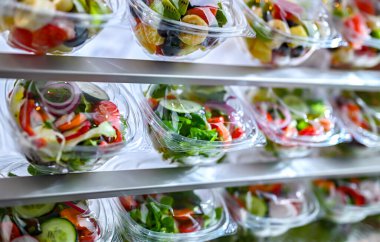 Önceden paketlenmiş meyve ve sebze salatalarıyla dolu plastik kutular ticari bir buzdolabında satılıyor.