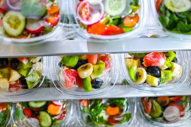 Önceden paketlenmiş meyve ve sebze salatalarıyla dolu plastik kutular ticari bir buzdolabında satılıyor.